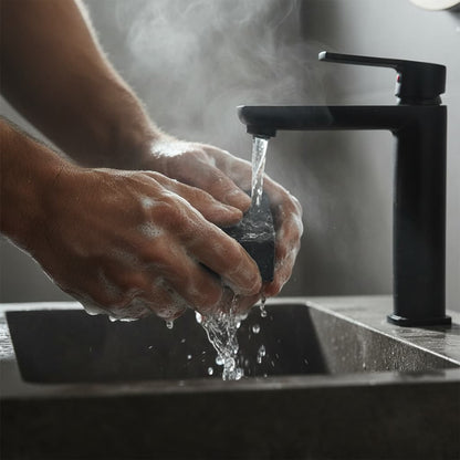 Person washing hands under a black faucet with steam in a blurred background