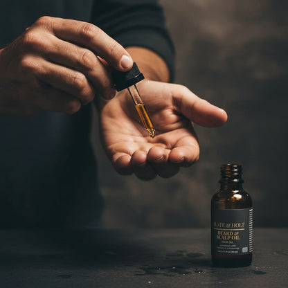 Hand holding a dropper with a small bottle of oil on a dark background